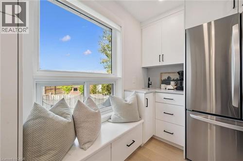 Built-in window bench with integrated storage, white cabinetry, stainless steel refrigerator, undermount sink with a matte black faucet, and light wood-finish flooring - 6 Branwood Place, Kitchener, ON 