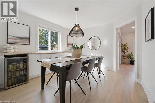 Dining area featuring wood-finish flooring, a beverage cooler, white cabinetry, a large window, and a modern pendant light fixture - 6 Branwood Place, Kitchener, ON 