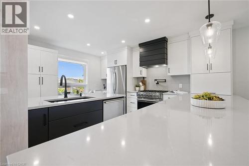 White cabinetry with black hardware, large kitchen island with light countertop, stainless steel refrigerator, stainless steel dishwasher, and a black range hood - 6 Branwood Place, Kitchener, ON 