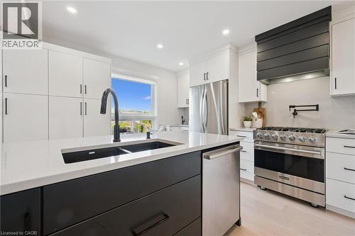 Kitchen featuring a central island with an undermount sink, stainless steel appliances, a black range hood, and light wood-finish flooring - 6 Branwood Place, Kitchener, ON 