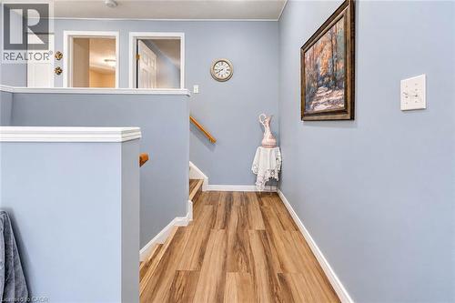 Wood-finish flooring throughout, white trim, light blue wall paint, and a wooden handrail on the staircase - 327 Oprington Place, Kitchener, ON 