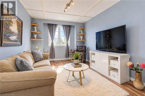 Recessed ceiling with track lighting, wood-finish flooring, built-in corner shelving, and a large window with white trim - 327 Oprington Place, Kitchener, ON 