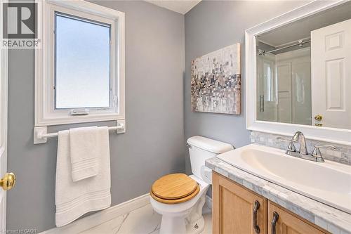 Single casement window, wood-finish vanity with chrome hardware, stone countertop, tile backsplash, and polished chrome faucet - 327 Oprington Place, Kitchener, ON 