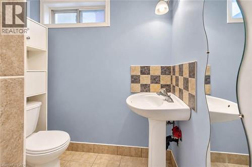 Pedestal sink with chrome faucet, checkerboard tile backsplash, and a wall-mounted curved mirror - 327 Oprington Place, Kitchener, ON 