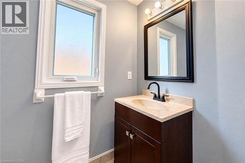 Single-pane window, dark wood-finish vanity with a light-toned countertop, integrated sink, and matte black faucet - 327 Oprington Place, Kitchener, ON 