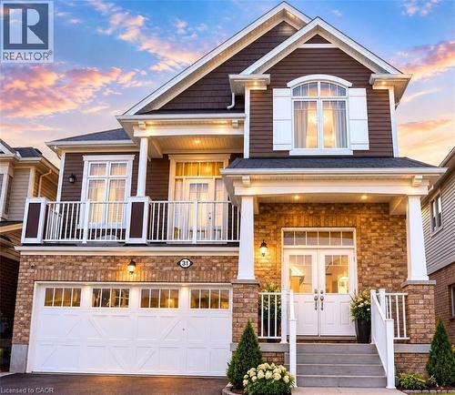Exterior facade featuring a combination of brick masonry and shake siding, a second-story balcony with metal railings, a double-car garage with carriage-style doors, and an elevated front porch - 31 Sofitel Drive, Kitchener, ON 