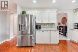 Kitchen featuring light-toned cabinetry, stone-finish countertops, stainless steel French-door refrigerator, tiled backsplash, and wood-finish flooring - 