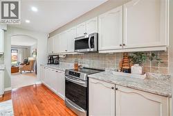 Kitchen featuring neutral-toned cabinetry, stone-finish countertops, stainless steel appliances, tiled backsplash, and wood-finish flooring - 