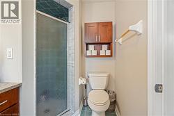 Shower featuring textured glass doors and stone-tiled interior, paired with wood-finish wall-mounted cabinetry and stone countertop - 