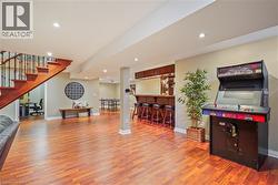 Open-concept interior featuring wood-finish flooring, recessed lighting, a built-in wet bar with cabinetry, and an exposed wooden staircase with metal balusters - 