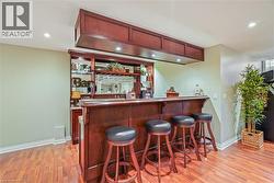 Custom wet bar featuring stained wood cabinetry, a mirrored backsplash, recessed overhead lighting, and wood-finish flooring - 