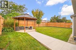 Backyard featuring a wooden gazebo with a shingled roof, a concrete walkway, a manicured lawn, and perimeter wood fencing - 