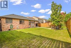 Backyard featuring a brick-exterior residence, a manicured lawn, a wooden privacy fence, and an integrated pergola structure - 