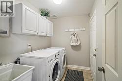 Utility room featuring white shaker-style wall cabinetry, a deep basin utility sink, tile flooring, and a wall-mounted hook rack - 