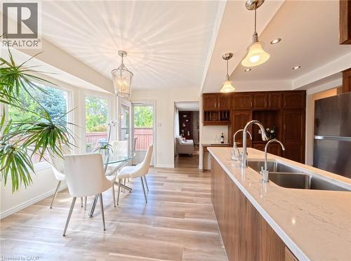 Kitchen featuring wood-finish cabinetry, an island with a light-toned solid surface countertop and undermount double-basin stainless steel sink, wood-finish flooring, and pendant lighting - 488 Heather Hill Place, Waterloo, ON 