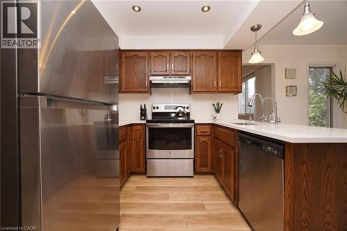 Kitchen featuring wood cabinetry, stainless steel appliances, white solid-surface countertops, wood-finish flooring, and pendant lighting - 488 Heather Hill Place, Waterloo, ON 