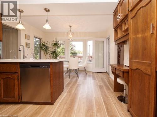 Kitchen featuring wood cabinetry, a stainless steel dishwasher, a built-in desk, pendant lighting, and wood-finish flooring - 488 Heather Hill Place, Waterloo, ON 