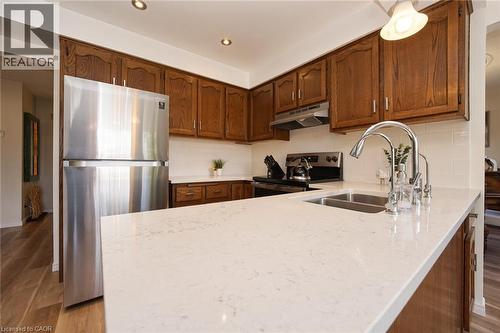 Kitchen featuring wood cabinetry, stone-finish countertops, stainless steel refrigerator, recessed lighting, and dual-basin undermount sink with a high-arch pull-down faucet - 488 Heather Hill Place, Waterloo, ON 