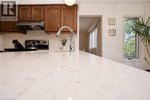 Kitchen featuring a stone-look countertop, stainless steel faucet, wood cabinetry, built-in range hood, and a vertical window - 488 Heather Hill Place, Waterloo, ON 