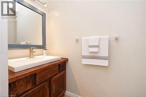 Wood-finish cabinetry vanity featuring a rectangular integrated sink, metallic finish faucet, wall-mounted mirror with a dark frame, and attached towel bar - 488 Heather Hill Place, Waterloo, ON 