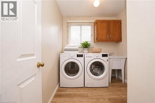 Laundry space featuring wood-finish flooring, a wall-mounted wood cabinet, a white utility sink, and horizontal window blinds - 488 Heather Hill Place, Waterloo, ON 