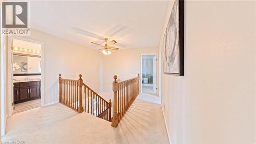 Carpeted hallway featuring wooden balustrade staircase railing and a multi-blade ceiling fan with integrated lighting - 488 Heather Hill Place, Waterloo, ON 
