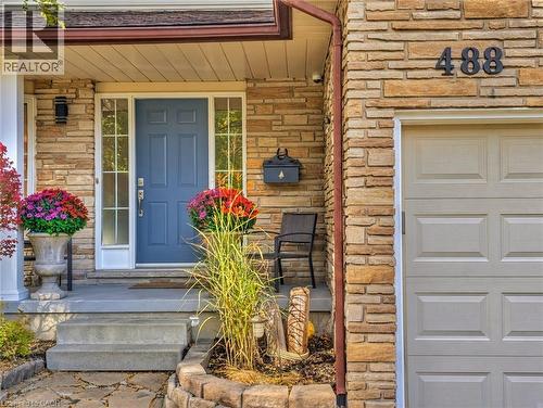 Stone veneer exterior featuring a covered porch, blue-painted panel door with sidelights, concrete steps, and a multi-section garage door - 488 Heather Hill Place, Waterloo, ON 