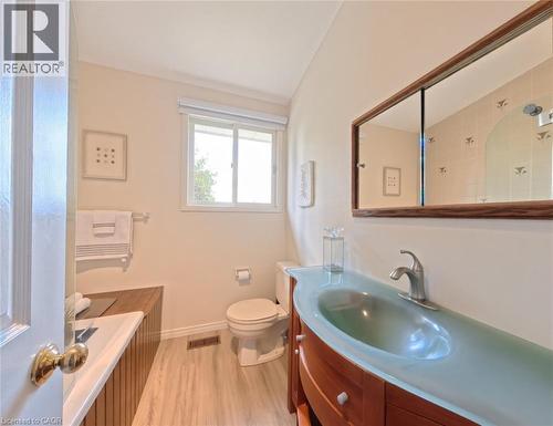Custom wood-finish vanity with a curved glass integrated sink, brushed metal faucet, light-toned wood-finish flooring, and a large framed mirror - 488 Heather Hill Place, Waterloo, ON 