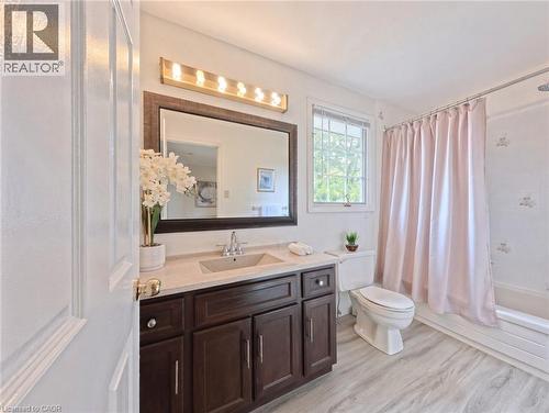 Bathroom featuring a vanity with dark-finish cabinetry, an integrated sink, a rectangular mirror with a dark frame, a multi-bulb light fixture, and wood-finish flooring - 488 Heather Hill Place, Waterloo, ON 