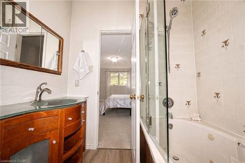 Curved wood vanity with glass countertop, integrated vessel sink, wall-mounted mirror, and glass-enclosed soaking tub with wall-mounted shower head - 488 Heather Hill Place, Waterloo, ON 