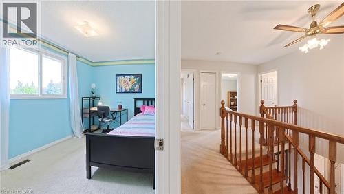 Interior space featuring neutral carpeting, a wood-finish staircase railing with balusters, a ceiling fan with integrated lighting, and multiple interior doors - 488 Heather Hill Place, Waterloo, ON 