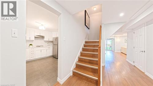 Staircase featuring wood-finish treads and a natural wood handrail, white cabinetry with integrated stainless steel appliances, and wood-finish flooring - 488 Heather Hill Place, Waterloo, ON 