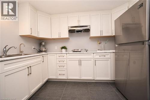 Kitchen featuring white cabinetry, stone-finish countertops, stainless steel appliances, a double-basin undermount sink, and large-format tile flooring - 488 Heather Hill Place, Waterloo, ON 