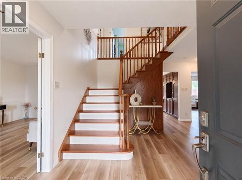 Foyer featuring wood-finish flooring, a staircase with a stained wood handrail and balusters, and built-in cabinetry - 488 Heather Hill Place, Waterloo, ON 