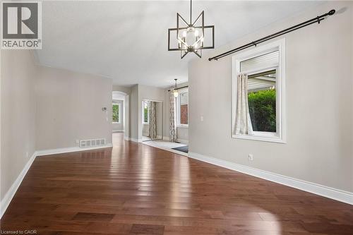 Open living area featuring wood-finish flooring, geometric-style metal chandelier, mirrored closet doors, and neutral wall tones - 83 Glazebrook Crescent, Cambridge, ON 