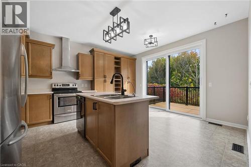 Kitchen featuring wood cabinetry, a central island with a dual-basin sink and high-arc faucet, stainless steel appliances, geometric pendant lighting, and sliding glass doors with access to an exterio - 83 Glazebrook Crescent, Cambridge, ON 