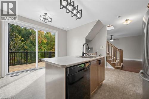 Kitchen island with a dual-basin sink and matte black faucet, sliding glass door leading to a wooden deck, geometric pendant lighting, and a staircase featuring wood-capped railing - 83 Glazebrook Crescent, Cambridge, ON 
