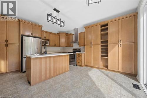 Kitchen featuring extensive wood-finish cabinetry, a central island with a white countertop, stainless steel appliances, a modern chimney-style range hood, and geometric pendant lighting - 83 Glazebrook Crescent, Cambridge, ON 