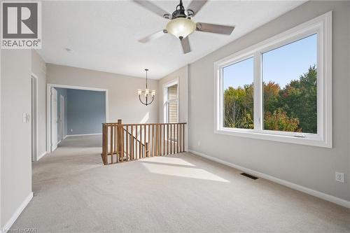 Neutral-toned carpeting, large picture window with outdoor scenery, wooden stair railing, ceiling fan with integrated lighting, and multi-arm chandelier - 83 Glazebrook Crescent, Cambridge, ON 