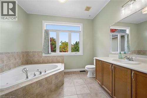 Corner soaking tub with tile surround, vanity with surface-mounted sink, tile flooring, and large window - 83 Glazebrook Crescent, Cambridge, ON 