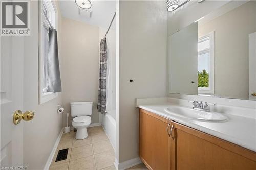 Bathroom featuring a wood-toned vanity with an integrated oval sink, solid-surface countertop, full-width vanity mirror, tile flooring, and a shower-tub combination - 83 Glazebrook Crescent, Cambridge, ON 