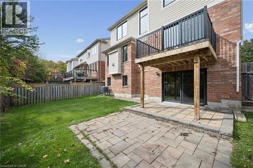 Exterior rear elevation featuring a brick and vinyl siding facade, a raised balcony with metal railing, a paved stone patio, and a fenced yard - 83 Glazebrook Crescent, Cambridge, ON 