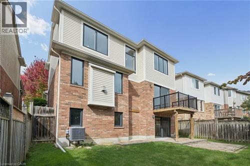 Two-story exterior featuring a brick and siding facade, an elevated wooden deck with metal railing, and a stone patio - 83 Glazebrook Crescent, Cambridge, ON 