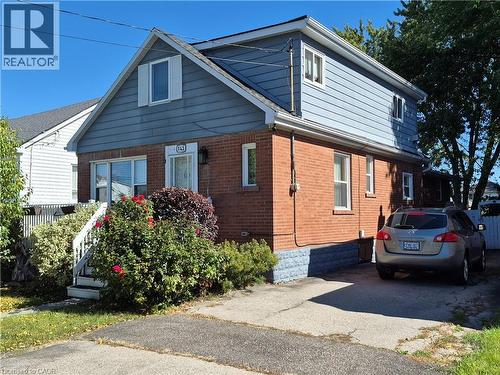 Exterior featuring red brick lower masonry, blue horizontal siding, white window trim, and a paved private driveway - 143 Walter Avenue S, Hamilton, ON 