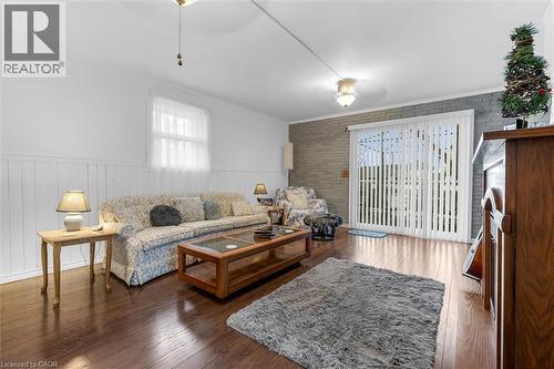 Bright living room featuring hardwood flooring, a brick accent wall, and abundant natural light from multiple windows - 143 Walter Avenue S, Hamilton, ON 