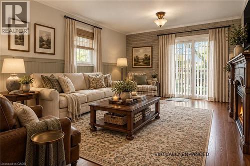 Living space featuring wood-finish flooring, a painted brick accent wall, wainscoting, a traditional fireplace surround, and sliding glass doors - 143 Walter Avenue S, Hamilton, ON 