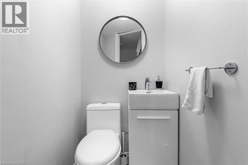 Wall-mounted round mirror, square pedestal-style vanity with built-in storage, chrome-finished faucet, and standard porcelain toilet - 143 Walter Avenue S, Hamilton, ON 