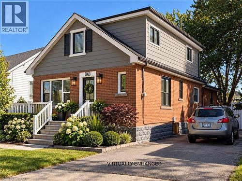 Two-story exterior featuring a brick facade with horizontal siding, a raised front porch with white railings, and an asphalt driveway - 143 Walter Avenue S, Hamilton, ON 
