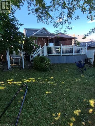 Rear exterior featuring brick siding, a raised deck with white railing, and a fenced backyard with mature trees - 143 Walter Avenue S, Hamilton, ON 