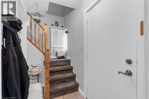 Entryway featuring a wood staircase with balusters, built-in louvered wall cabinet, and tile flooring - 143 Walter Avenue S, Hamilton, ON 